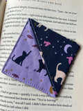 Two fabric bookmarks with cat designs on a book page.