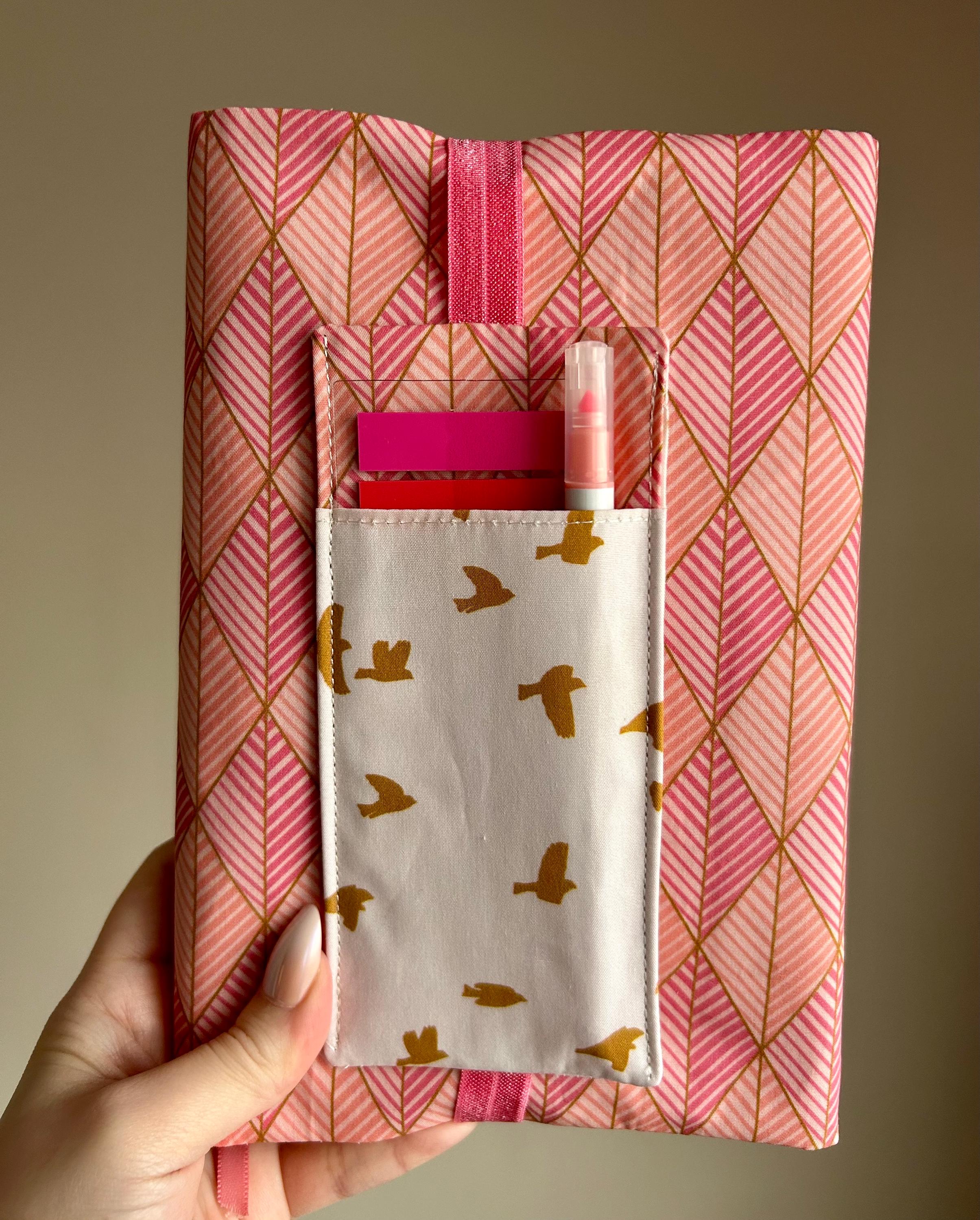Pink geometric patterned pouch with a smaller pocket featuring bird design, held against a beige background.