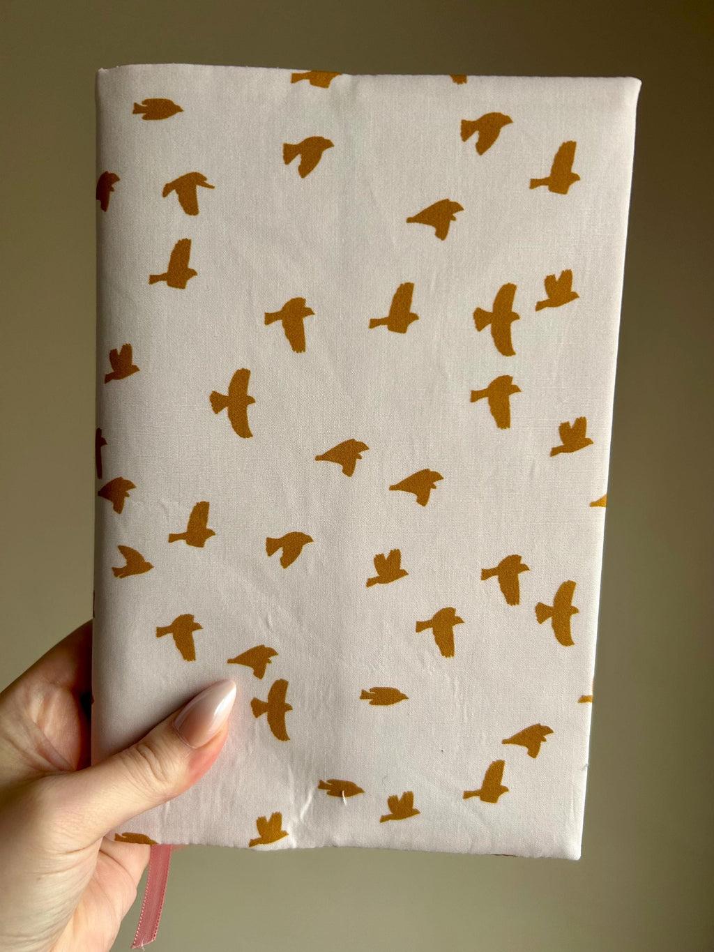 Notebook with gold bird pattern held by a hand against a beige background