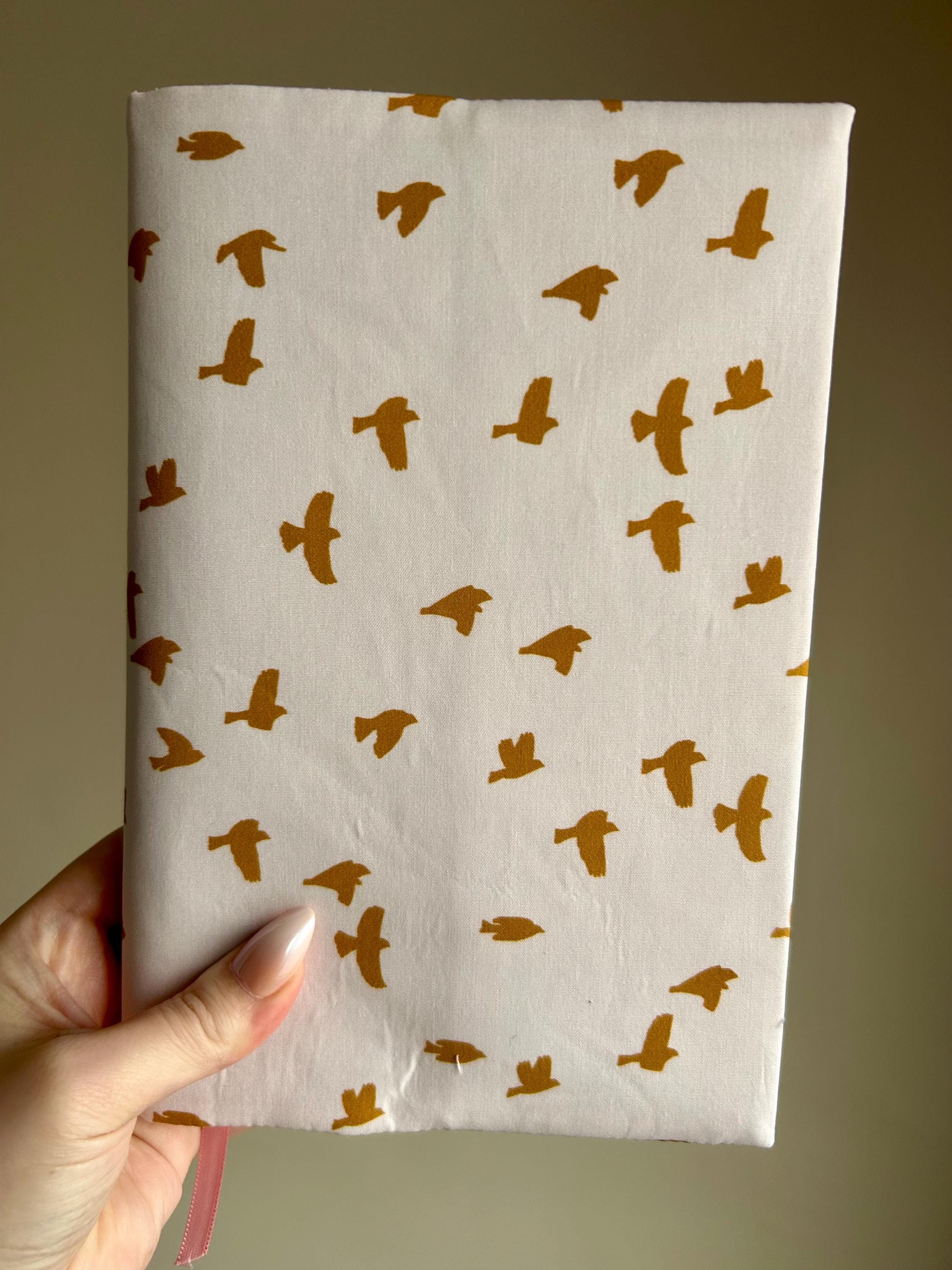Notebook with gold bird pattern held by a hand against a beige background