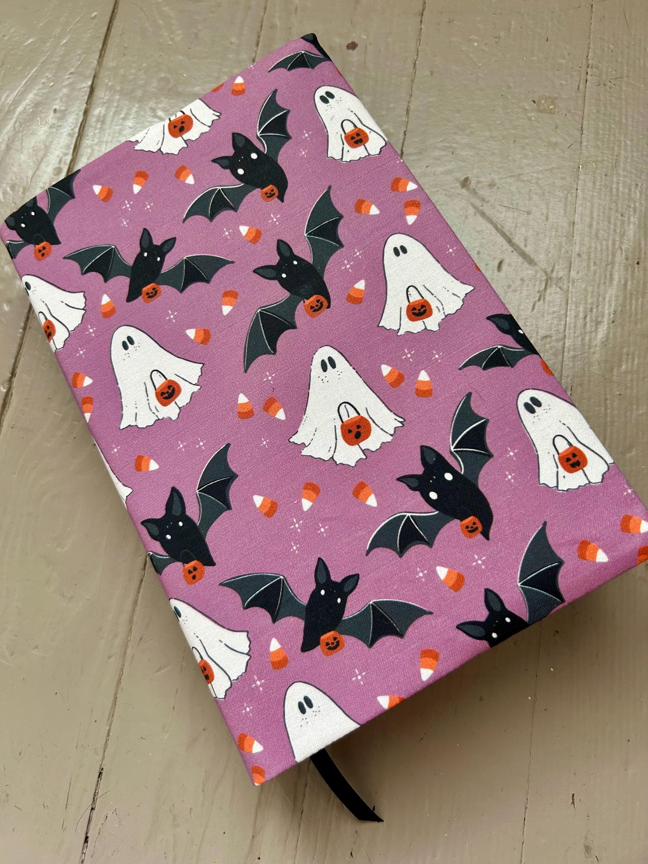 Halloween-themed notebook with ghost, bat, and candy corn pattern on a pink background.